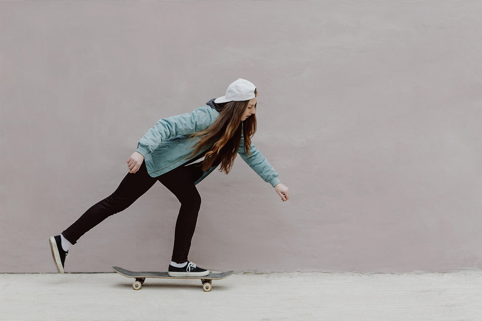 Garota andando de skate em parede rosa
