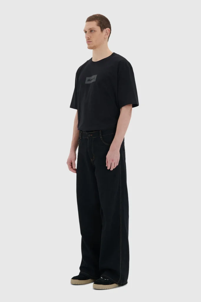 Homem em camiseta preta e calça larga preta.