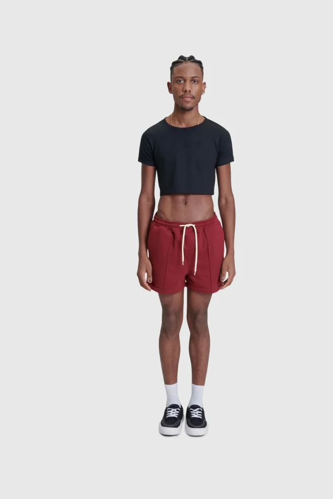 Modelo masculino usando camiseta cropped e bermuda vermelha.
