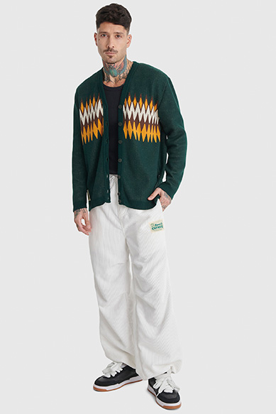 Modelo masculino com cardigan verde e calças brancas.