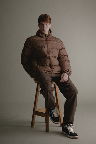 Modelo masculino com jaqueta marrom sentado em um banco