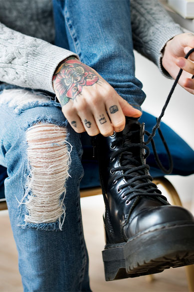 Pessoas amarrando bota de couro preta com jeans rasgado.