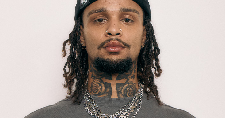 Homem com cabelo encaracolado e tatuagens visíveis.