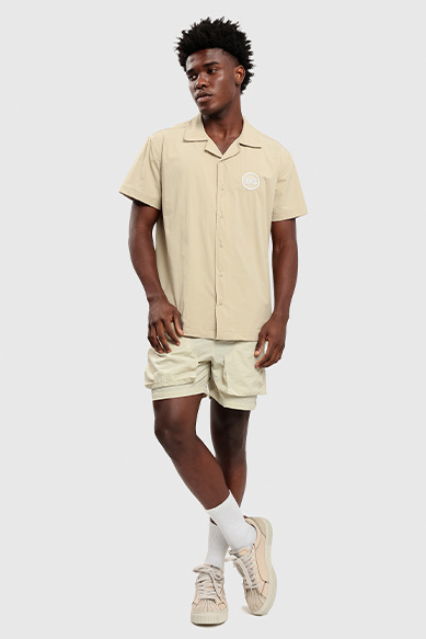 Homem com camisa bege e shorts claros em pé