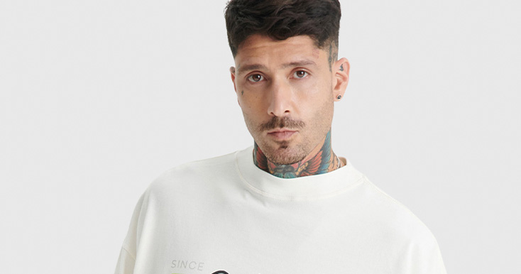 Homem com camiseta branca e tatuagens visíveis