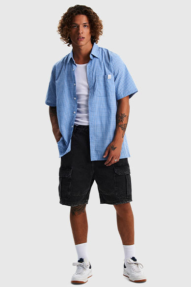 Jovem modelo com camisa xadrez azul e bermuda preta.