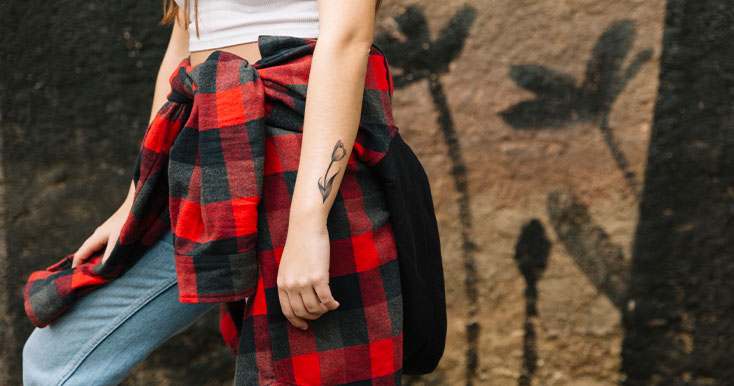 Jovem com roupa xadrez e tatuagem em mural urbano