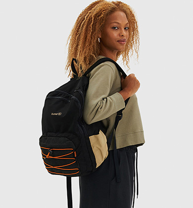 Mulher com mochila preta e detalhes em laranja.