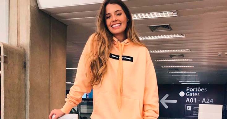 Modelo sorrindo com moletom rosa em aeroporto