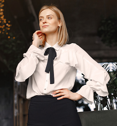 Mulher loira com blusa branca e laço preto em ambiente interno