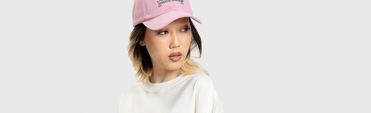 Mulher usando boné rosa e camiseta branca.