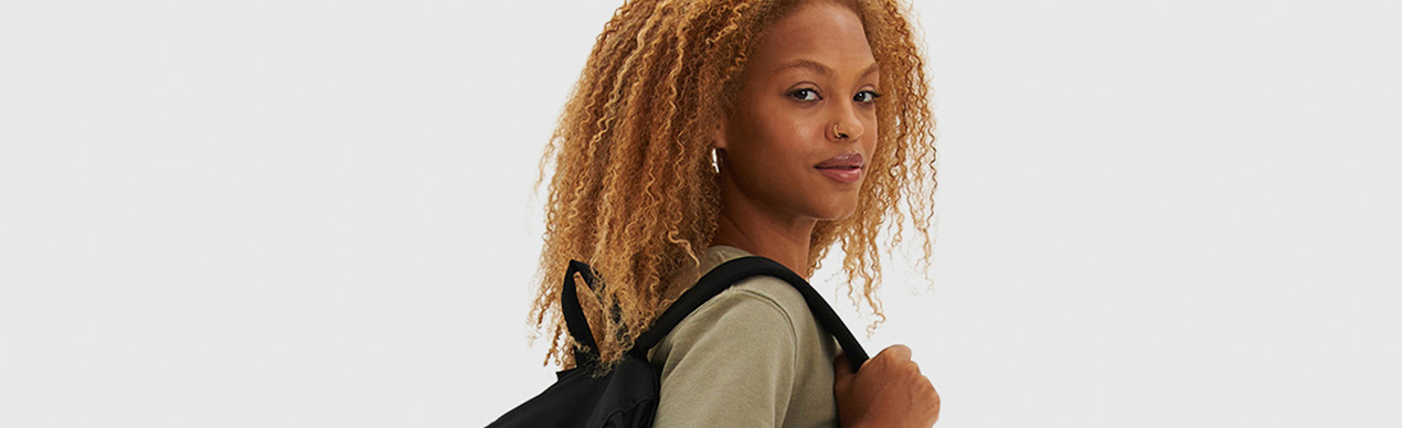 Jovem mulher com cabelo cacheado mostrando mochila preta