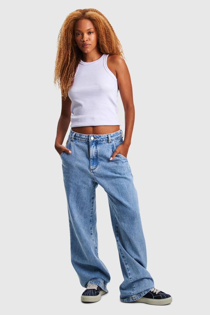 Mulher com cabelo cacheado usando calça jeans larga e top branco.