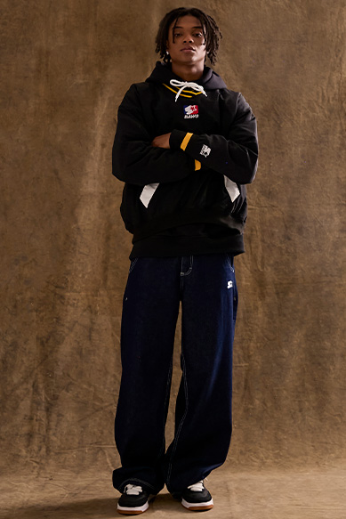 Jovem em moletom preto e calça larga, em fundo neutro.