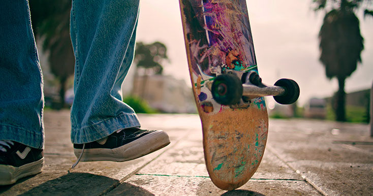 Pé com tênis preto sobre um skate colorido