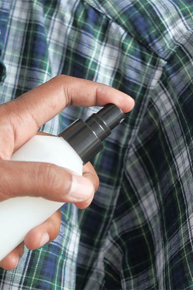 Pessoa aplicando produto em camisa xadrez.