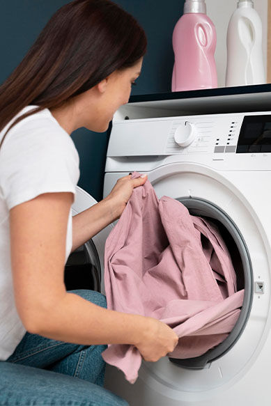 Mulher colocando roupa rosa na lavadora