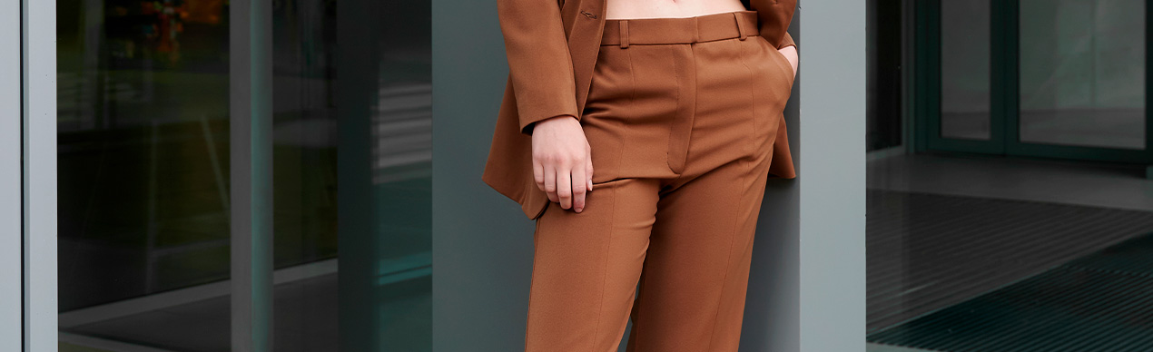 Modelo feminina com terno marrom em ambiente urbano.